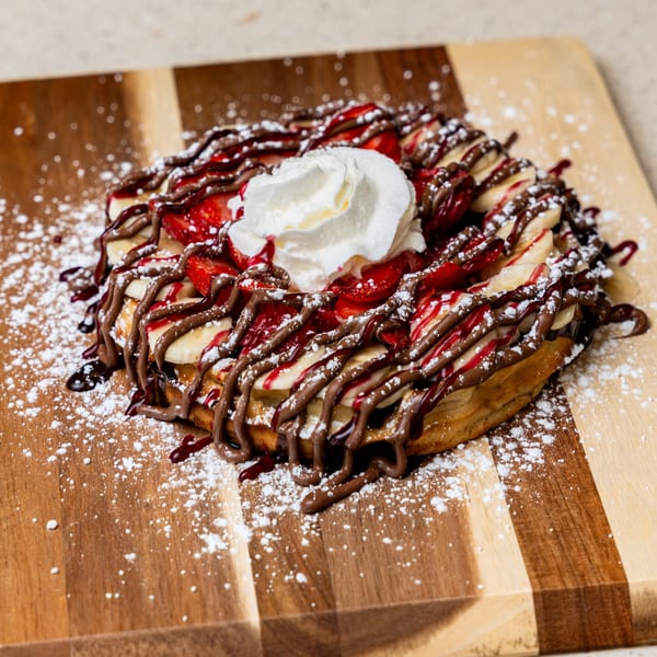 Crepe topped with strawberries, bananas, chocolate drizzle, strawberry syrup, whipped cream, and powdered sugar.