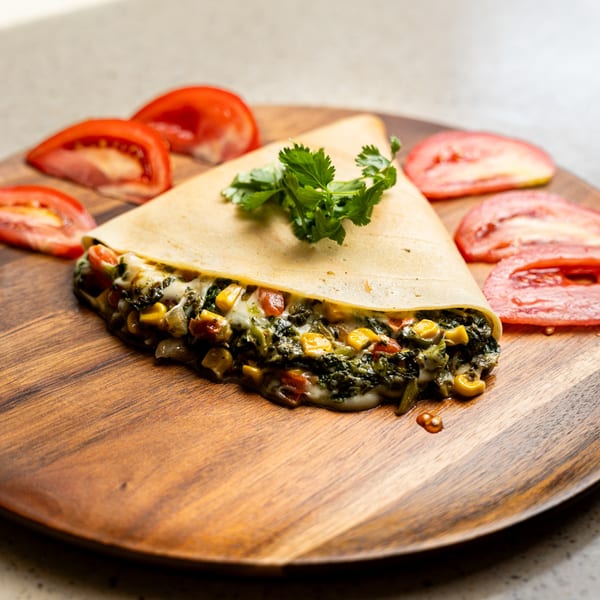 Savory crepe filled with spinach, corn, and melted cheese, garnished with cilantro and tomato slices.