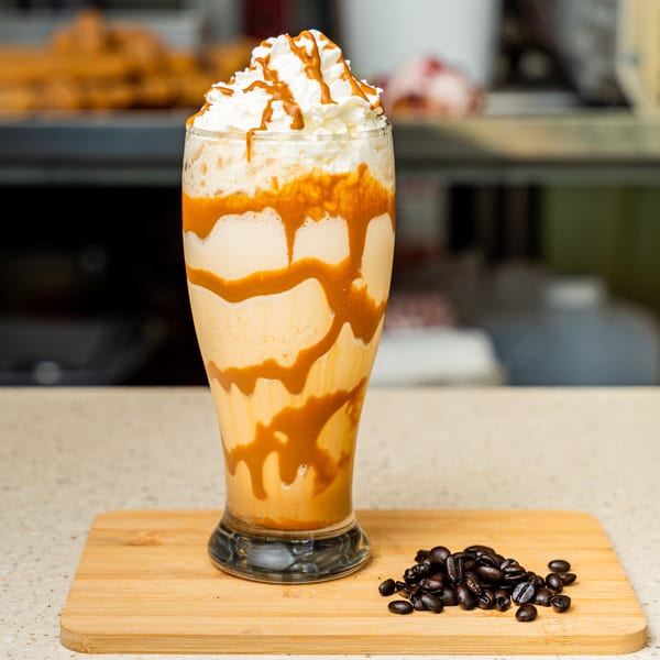Caramel frappe with whipped cream and caramel drizzle, next to coffee beans on a wooden board.