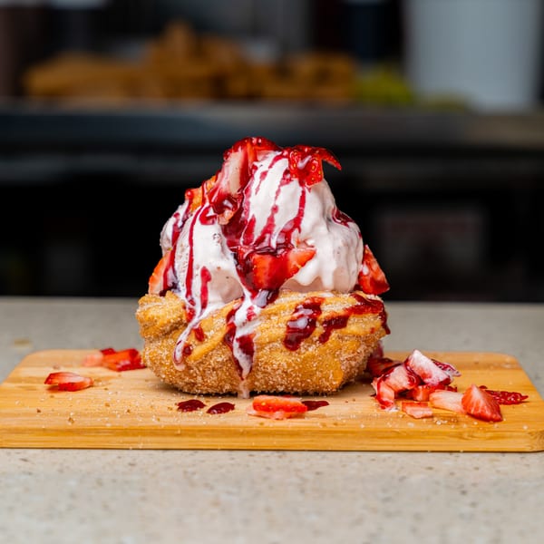 Churro bowl filled with vanilla ice cream, strawberry syrup, and fresh strawberries on a wooden board.